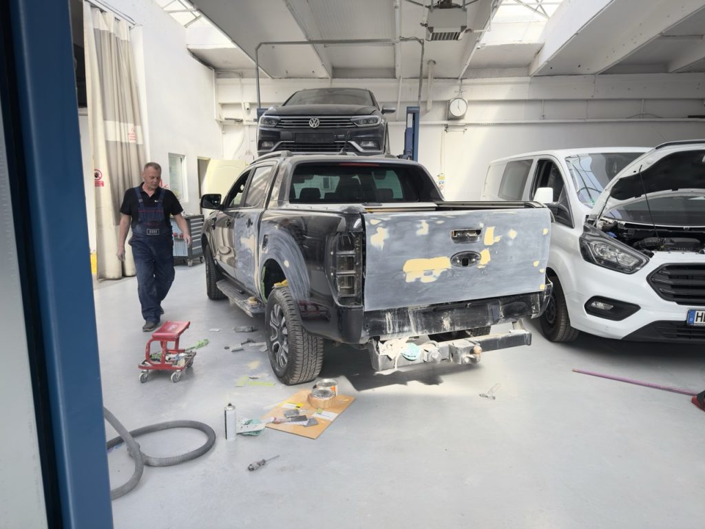 Tehnician auto lucrând într-un atelier de reparații auto din Fălticeni, în zona de tinichigerie, alături de un pick-up avariat.